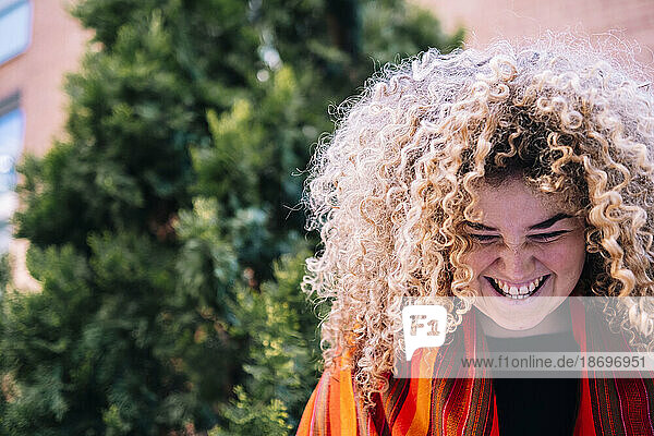 Junge Frau mit lockigem Haar lacht vor Baum