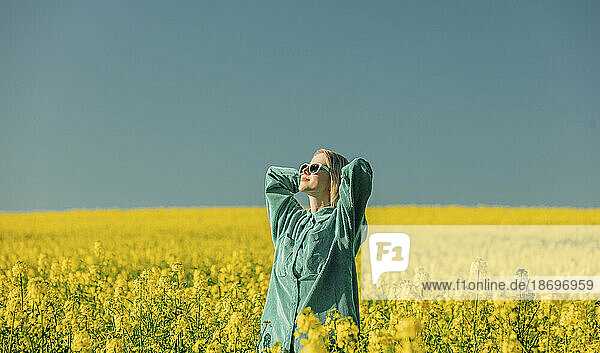 Woman with hands behind head standing in rapeseed field