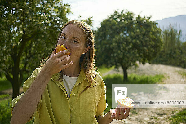 Frau isst saftige Orange im Obstgarten