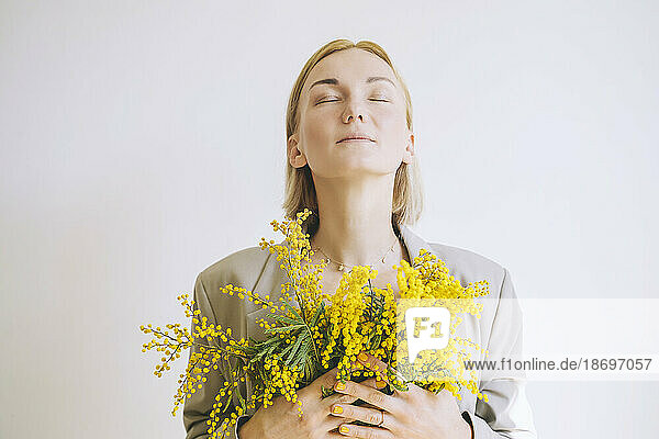 Woman with eyes closed holding mimosa flowers against white background