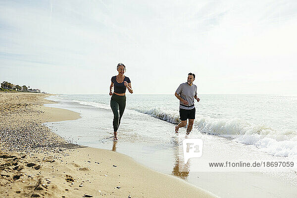 Mature couple running together by wave at beach