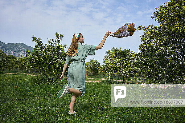 Woman playing with mesh bag on grass in orange orchard