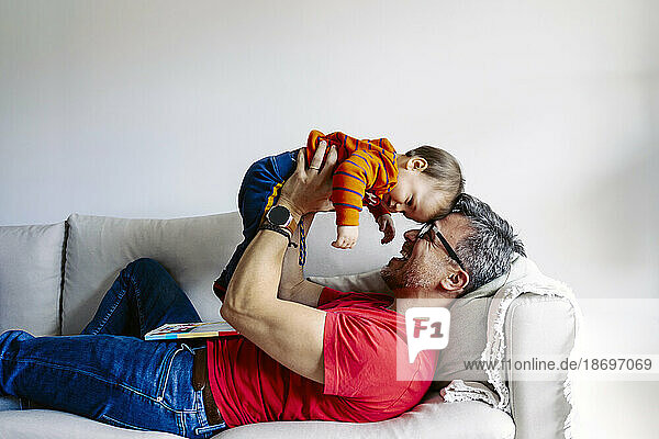 Glücklicher Vater  der zu Hause mit seinem Sohn auf dem Sofa spielt