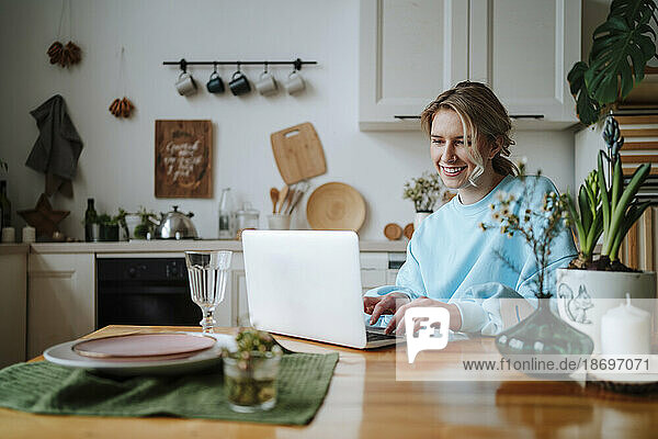 Lächelnde Frau benutzt Laptop in der heimischen Küche