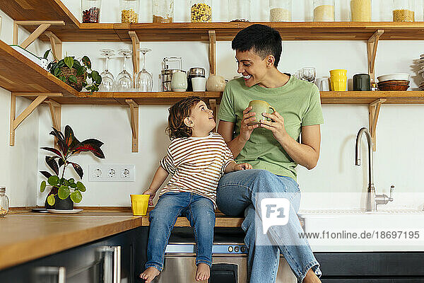 Happy woman sitting with son on kitchen counter at home