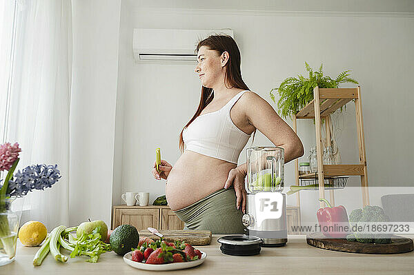 Schwangere Frau mit der Hand auf der Hüfte steht zu Hause in der Küche