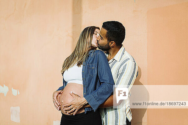 Pregnant woman kissing man near wall