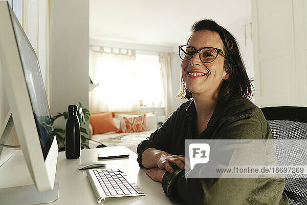 Smiling freelancer with computer at desk in home office