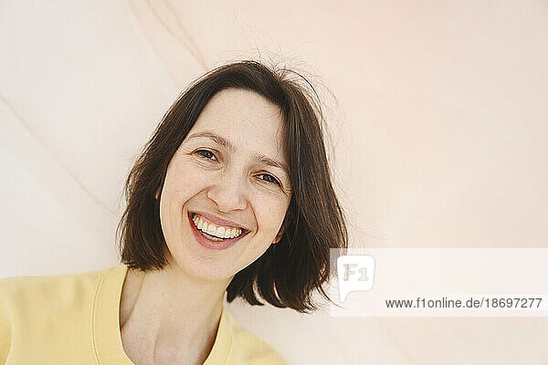 Smiling woman with short brown hair on pink background