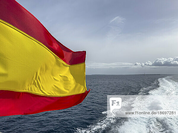 Spain  Balearic Islands  Formentera  Wake left by moving boat with Spanish flag fluttering in foreground