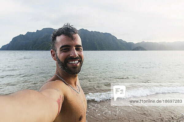 Happy shirtless man taking selfie at shore