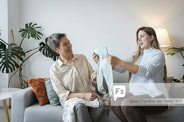 Woman and pregnant daughter choosing baby clothes at home