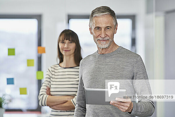 Confident businessman holding tablet PC with colleague at office