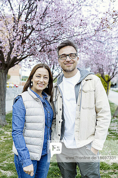Smiling couple standing together in front of cherry blossom tree
