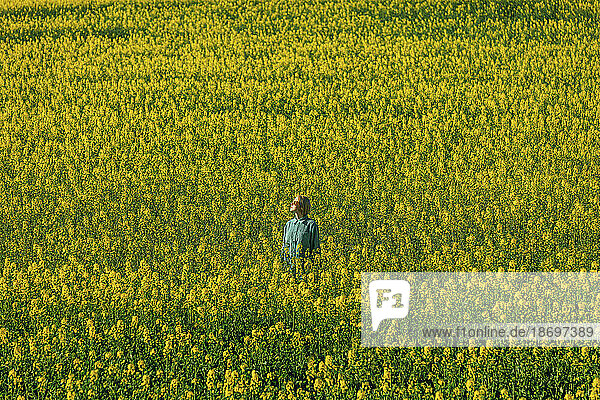 Woman standing amidst yellow rapeseed flowers in field