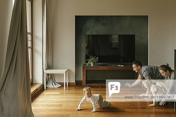 Playful family crawling on hardwood floor at home