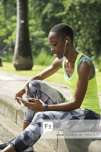 Frau surft mit Smartphone im Internet und sitzt auf Gehweg im Park