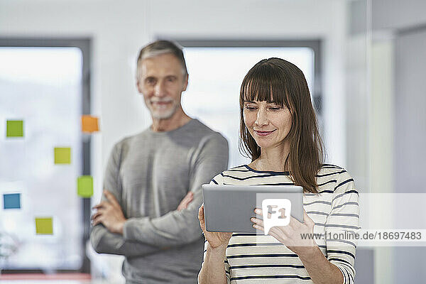 Businesswoman using tablet PC with colleague in background at office