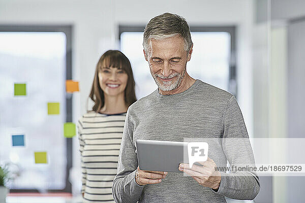 Businessman using tablet PC with colleague in background