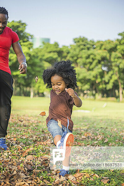 Son kicking dried leaves with father at park