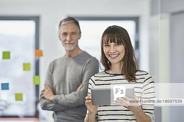 Happy businesswoman holding tablet PC with senior colleague in background