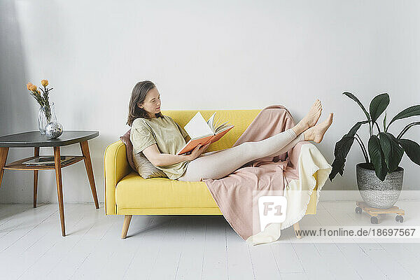 Woman reading book on yellow sofa in living room