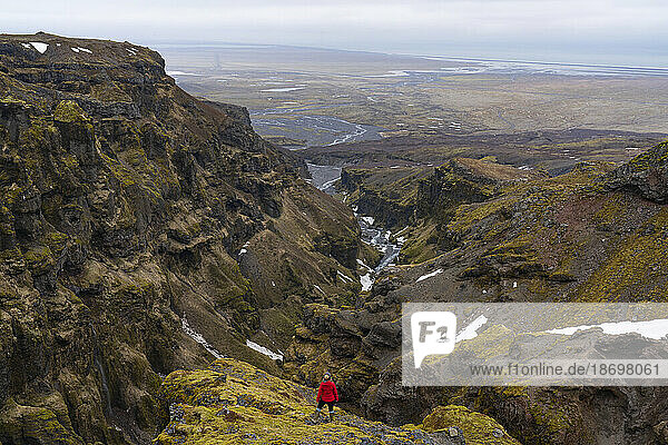 View taken from behind of a woman standing on a mountainside overlooking a vista of Mulagljufur Canyon  a hikers paradise  with an amazing view of a river winding through the moss-covered cliffs; Vik  South Iceland  Iceland