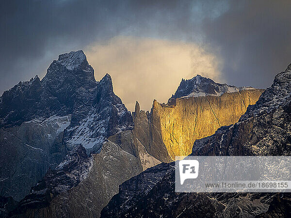 Sunlit rock faces of the jagged  mountain peaks in the Torres del Paine National Park under a stormy sky with storm light; Torres del Paine National Park  Patagonia  Chile
