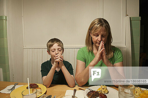 Mother and son sit at the kitchen table and pray before dinner; Lincoln  Nebraska  United States of America