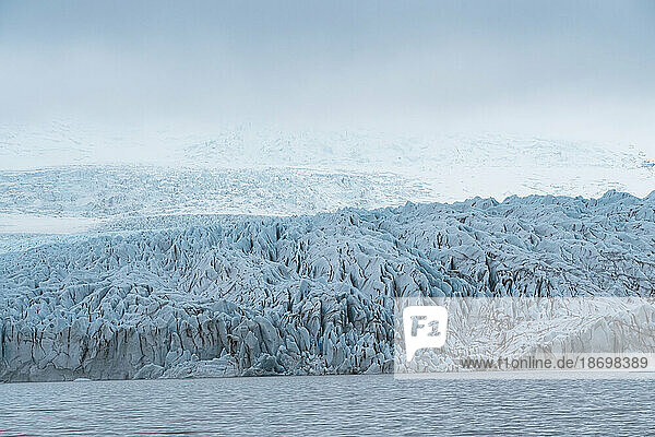 Views of the blue ice of the Fjallsjokull Glacier stands out in the misty atmosphere from the Fjallsarlon Glacier Lagoon  at the south end of the famous Icelandic glacier Vatnajökull in Southern Iceland; South Iceland  Iceland