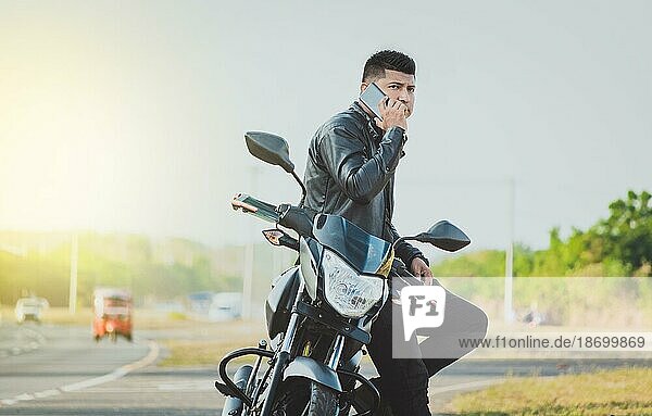 Biker sitting on motorcycle calling on the phone on the roadside. Handsome biker calling on the phone in the street. Concept of motorcyclist using the phone