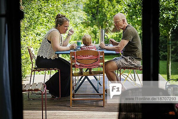 Familie sitzt gemeinsam auf der Terasse bei einer Mahlzeit.  Bonn  Deutschland  Europa