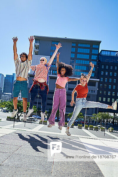 Portrait happy young friends jumping for joy in sunny city