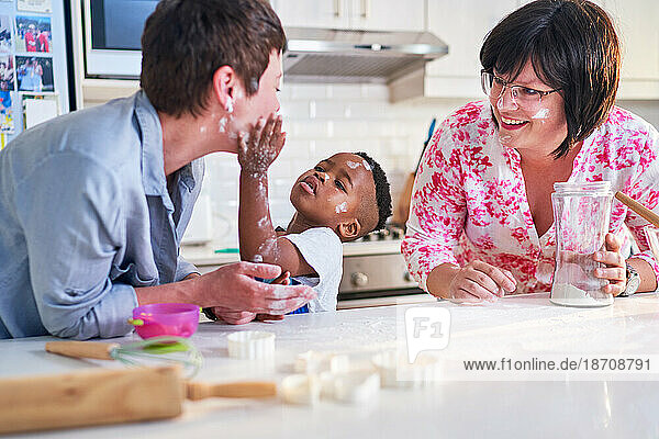 Playful  messy lesbian couple and son baking in kitchen at home