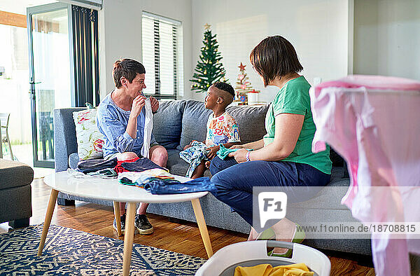 Lesbian couple and son folding laundry on living room sofa