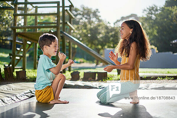Happy brother and sister playing clapping game on sunny trampoline