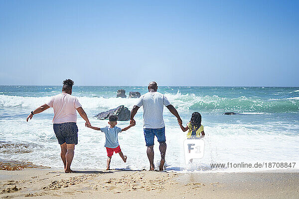 Gay male couple and kids holding hands  splashing in sunny ocean surf