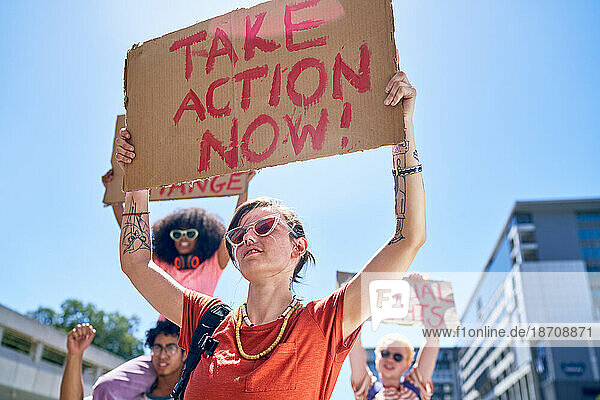 Young female protester holding action sign overhead in sunny city