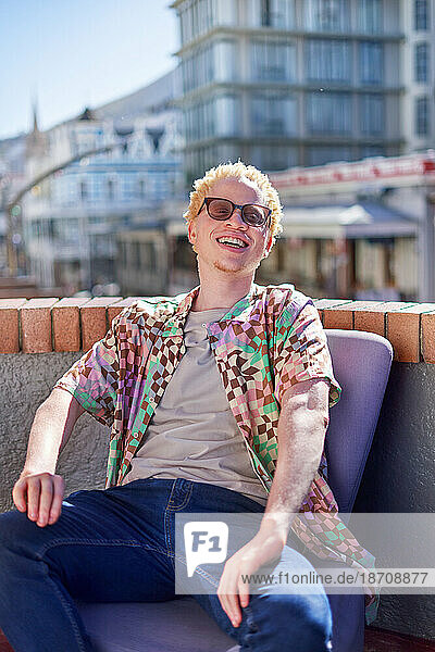 Portrait happy young albino man sitting on sunny city rooftop