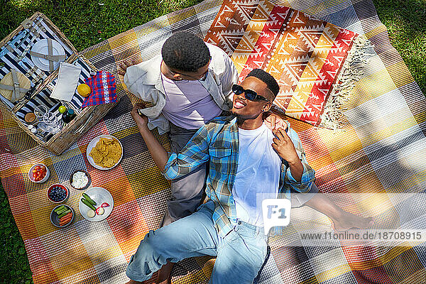 Young gay male couple cuddling  enjoying picnic on blanket in park