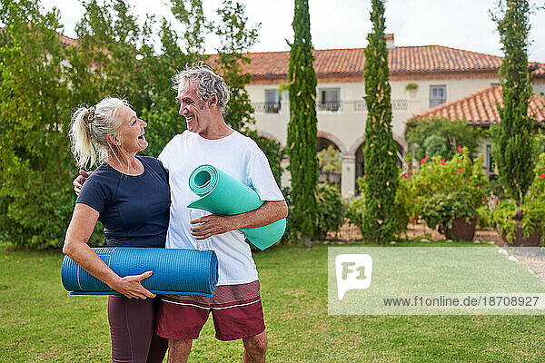 Happy senior couple with yoga mats in villa garden