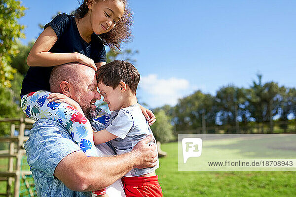 Father holding  carrying daughter and son with Down Syndrome in park