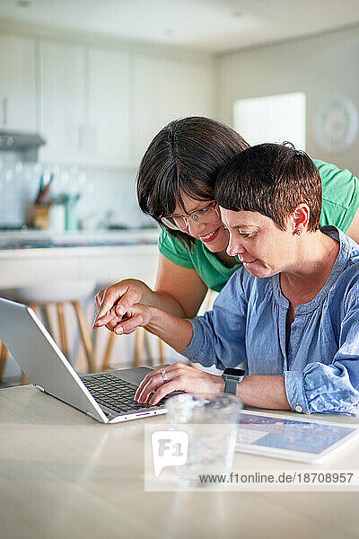 Happy lesbian couple using laptop in dining room at home