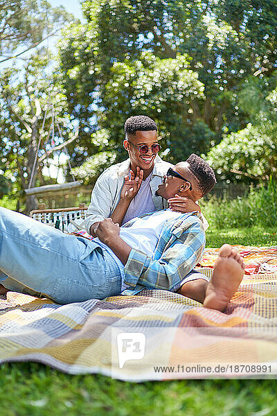 Happy young gay male couple cuddling on picnic blanket in park