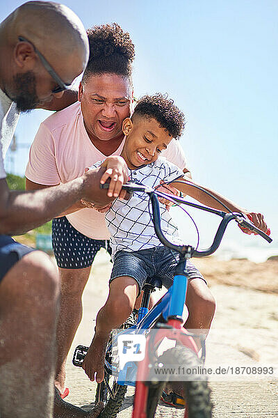 Happy gay male couple helping son riding bike on beach boardwalk