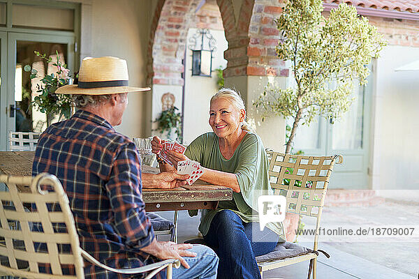 Happy senior couple playing card game at villa patio table