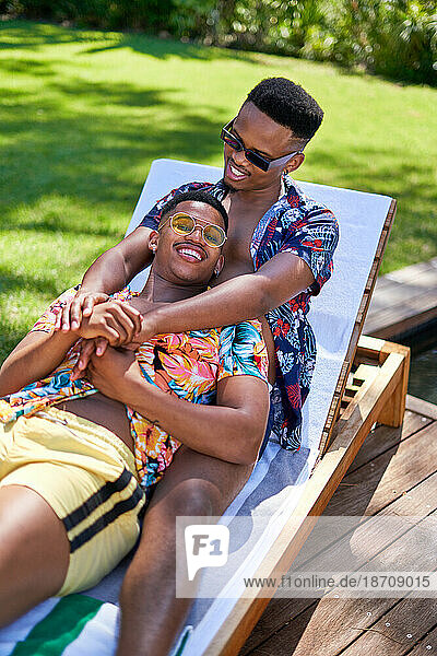 Happy young gay male couple cuddling  relaxing on lounge chair