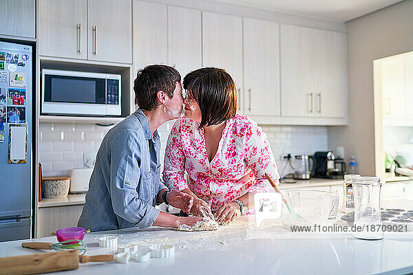 Affectionate lesbian couple baking  kissing in kitchen at home