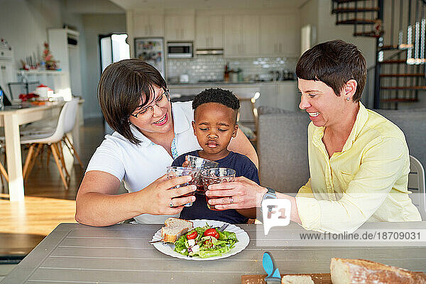Happy lesbian couple and son toasting drinking glasses at dinner table