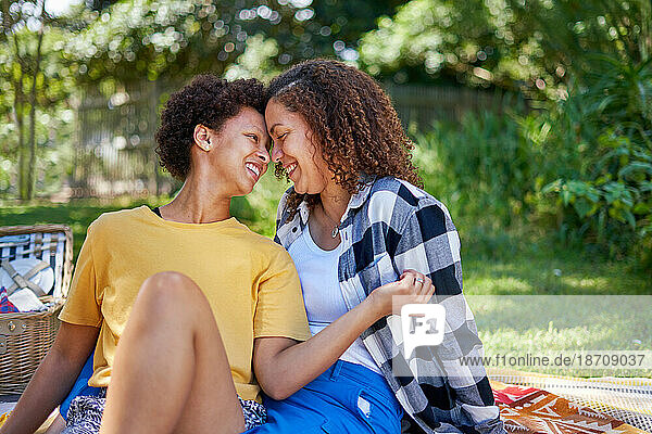 Happy  affectionate lesbian couple cuddling on picnic blanket in park